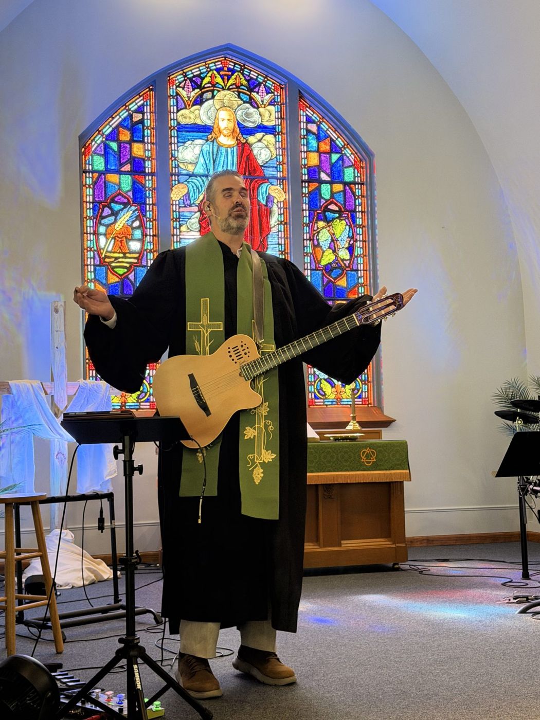Randy singing with an acoustic guitar in front of the stained-glass window