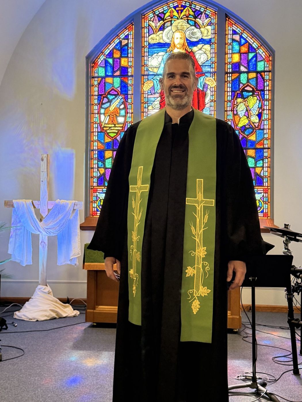 Randy Bennett, The Singing Pastor, smiling in a green stole in front of a stained-glass window